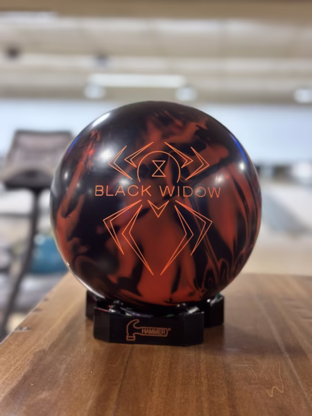 Close-up of Hammer Black Widow 3.0 bowling ball in red and black on wooden lane, premium performance ball for league and tournament bowlers