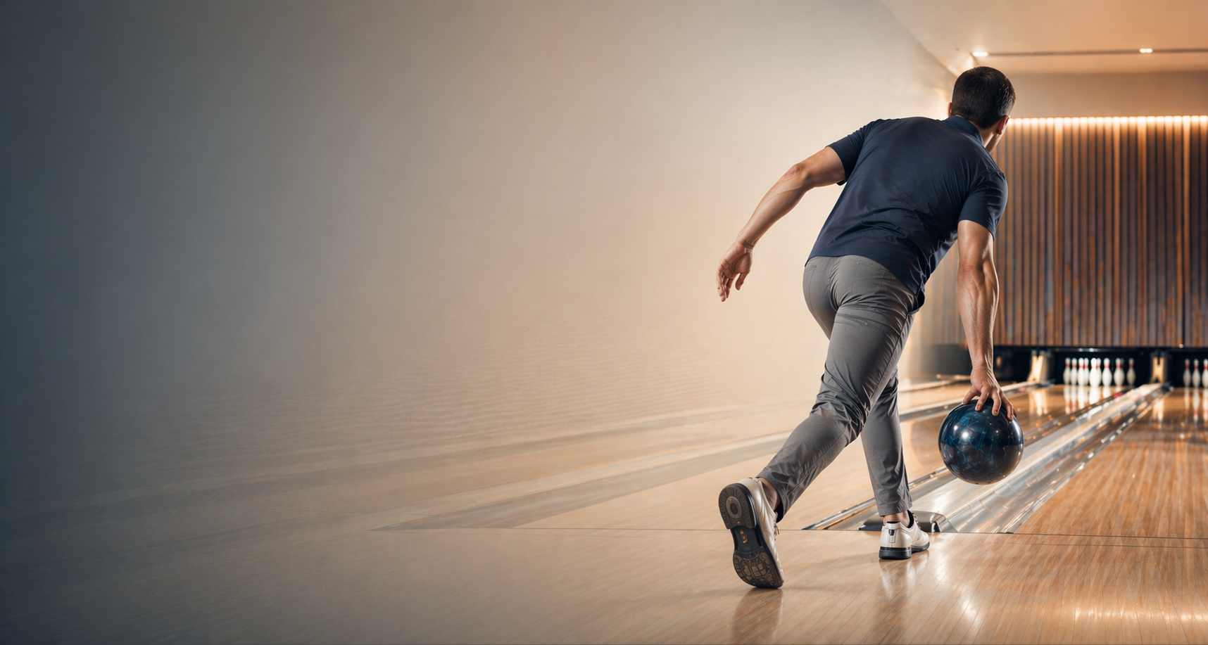 Bowler captured mid-stride on the approach holding a polished bowling ball, walking toward the foul line on hardwood lanes with bowling pins visible at the end — editorial sports photography of bowling technique